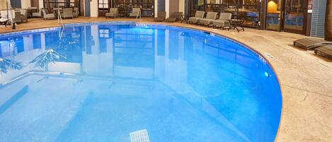 An indoor swimming pool with lounge chairs and a bar area.
