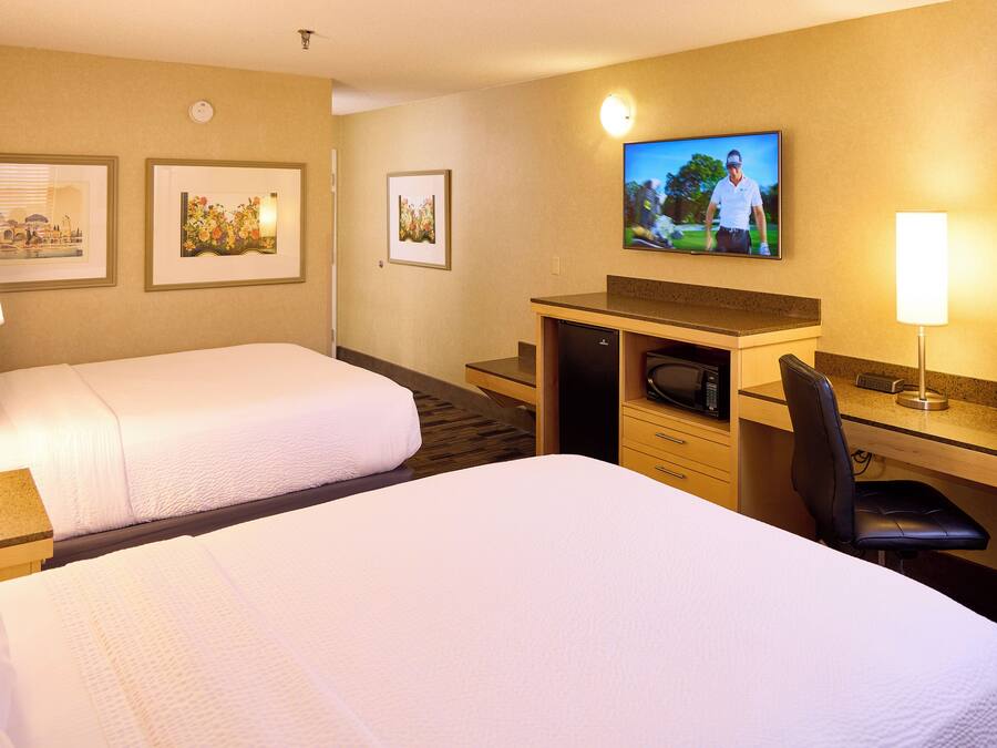 A hotel room with two beds, a desk with a microwave, a TV, and a chair.