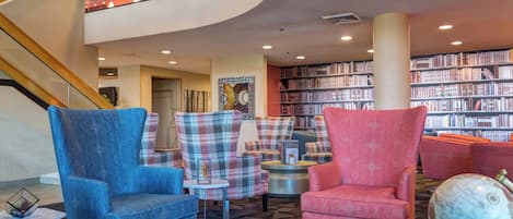 A modern library with a curved staircase, multiple seating areas, and a large collection of bookshelves.