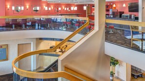Een moderne hotellobby met een centrale trap, zithoeken en een zichtbaar receptiebalie.