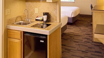 A compact hotel room with a kitchenette, including a microwave, sink, and dishwasher. There is a bed and a small desk area.