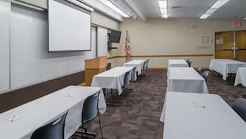 A conference room with white tables, chairs, a podium, a projector screen, and an American flag.