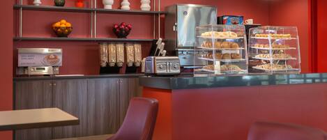 A modern cafe interior with a self-serve pancake station, a coffee machine, and a display of pastries.