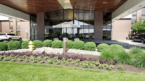 Entree van een LivInn hotel met een modern ontwerp, bestaande uit een overdekte inrit, een aangelegde tuin met een gele brandkraan en een parkeerplaats met auto's.