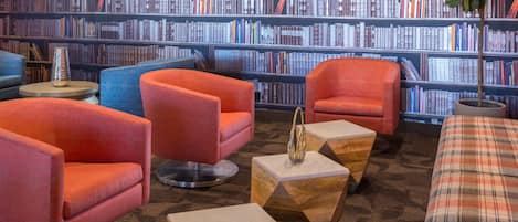 A library with multiple rows of bookshelves filled with books, several orange armchairs, and a plaid sofa.