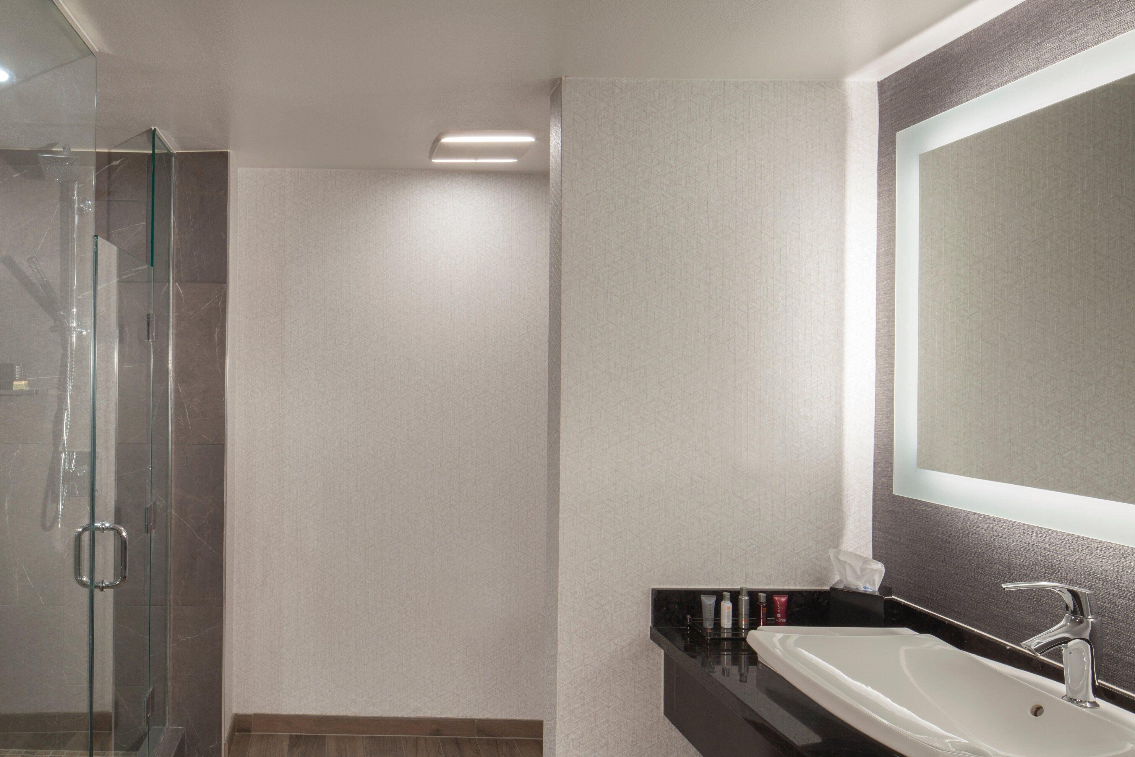Een moderne badkamer met een glazen douchecabine, een wit wastafeltje en een grote spiegel.