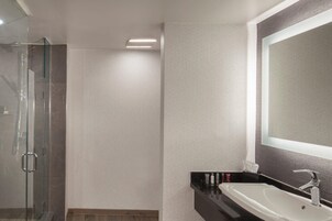 Een moderne badkamer met een glazen douchecabine, een wit wastafeltje en een grote spiegel.