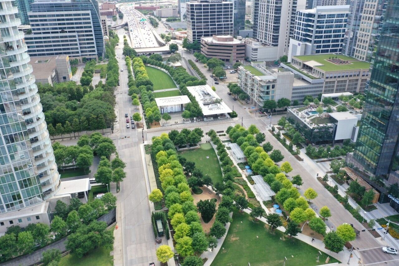An aerial view of a modern urban area with high-rise buildings, green spaces, and a central road.