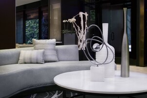 Een moderne woonkamer met een grijze bank, witte kussens, een ronde witte tafel en abstracte sculpturen.