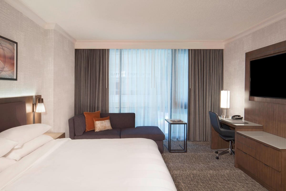 A hotel room with a large bed, a sofa, a desk, and a TV.