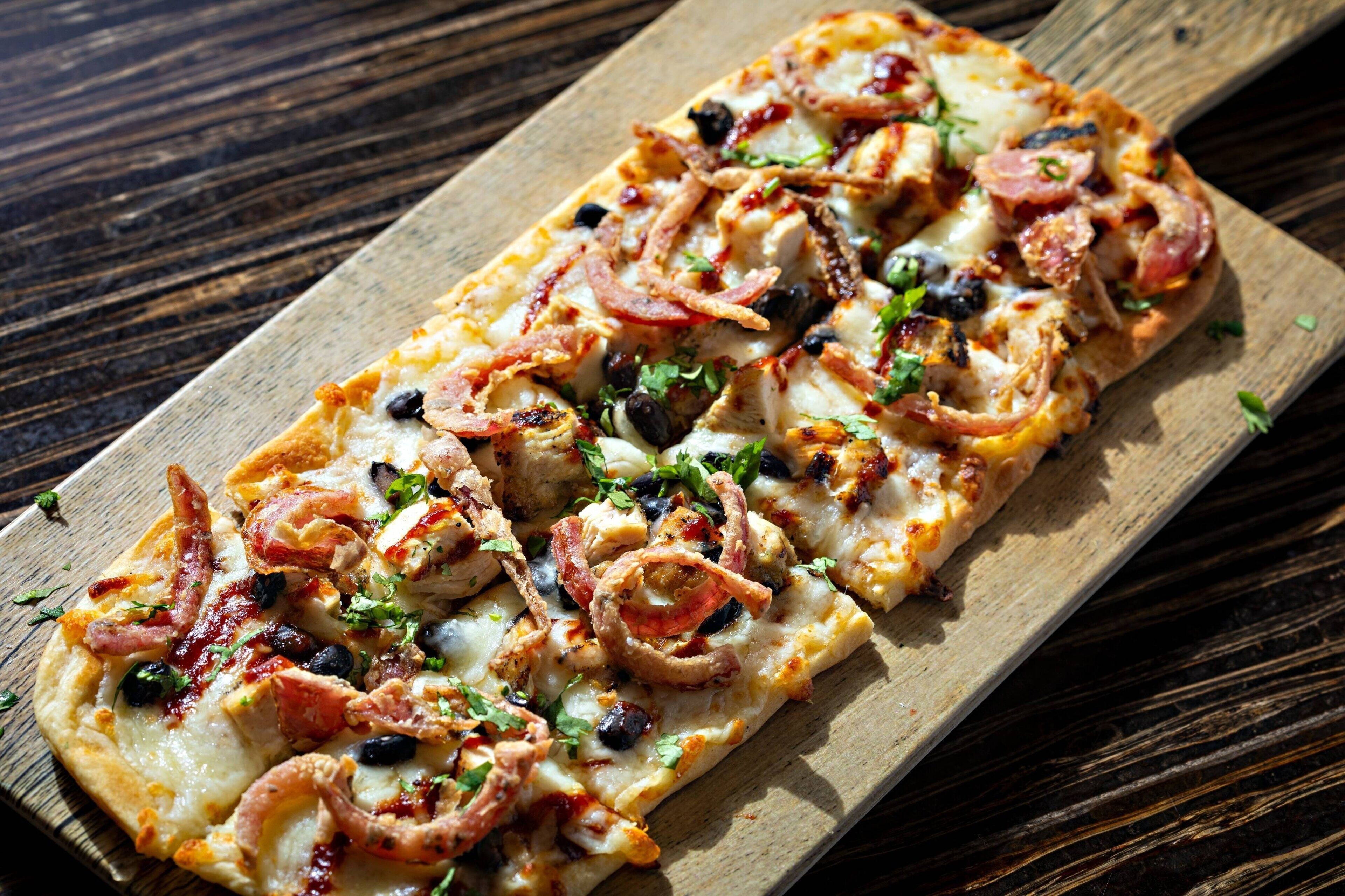 Une pizza rectangulaire, garnie de divers ingrédients, servie sur une planche en bois.