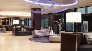 Um lobby moderno com design de teto circular, áreas de estar confortáveis e uma grande janela com vista para o exterior.