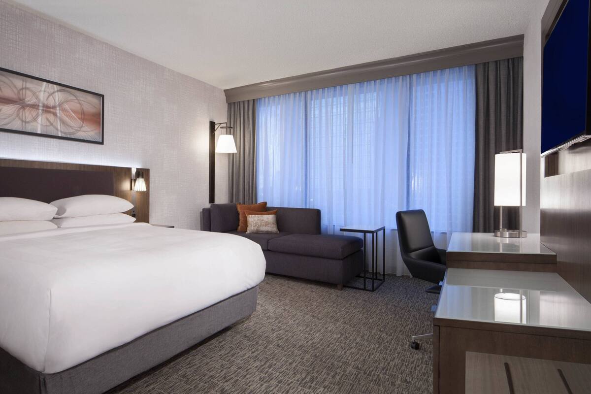 A hotel room with a large bed, a sofa, a desk, and a TV.