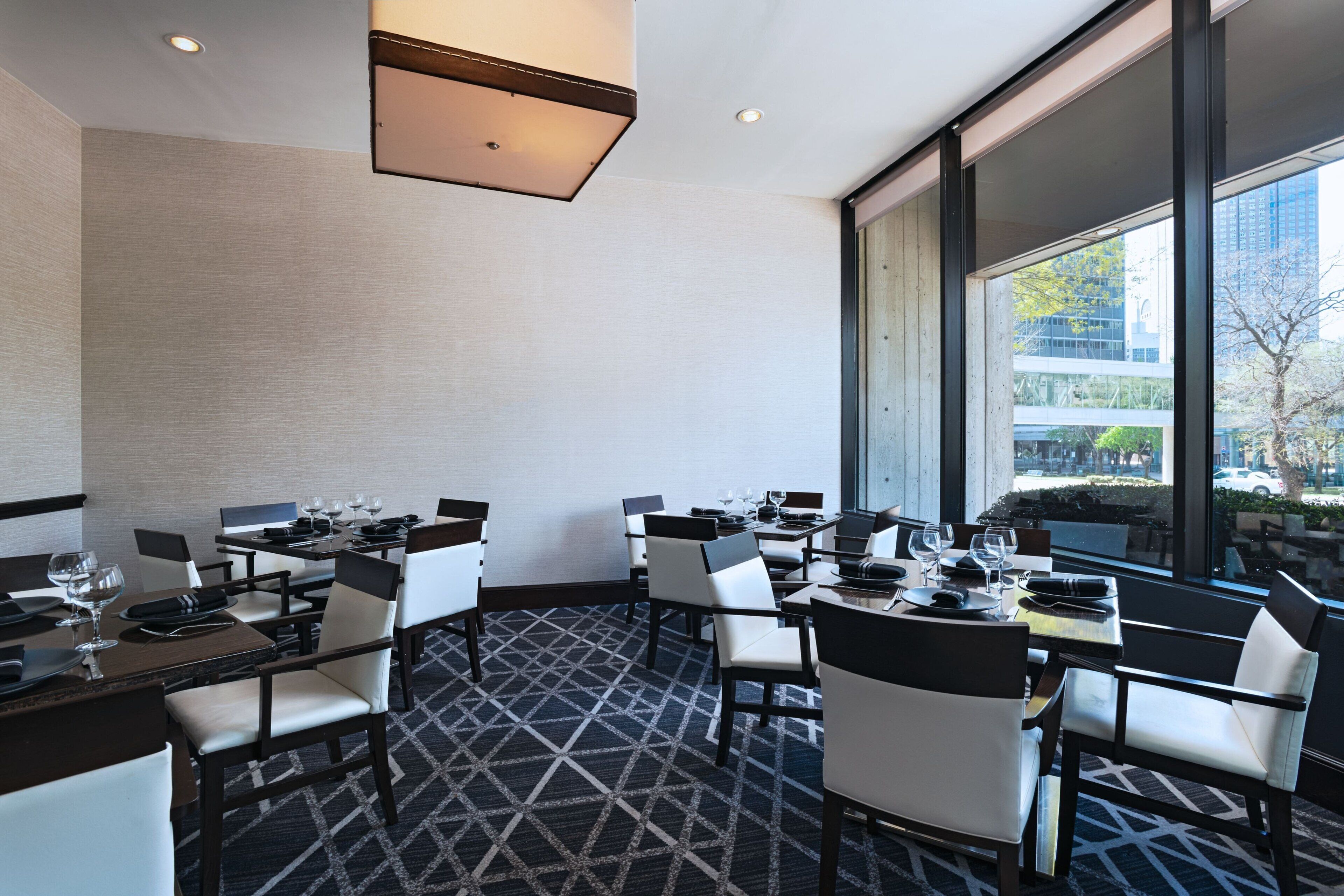 A dining area with tables and chairs, large windows, and a patterned carpet.