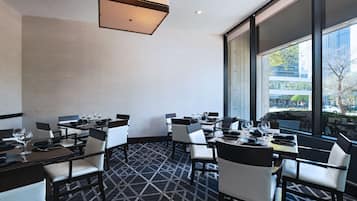A dining area with tables and chairs, large windows, and a patterned carpet.