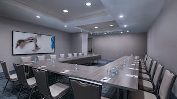 A conference room with a long table, chairs, and a projector screen displaying an image.