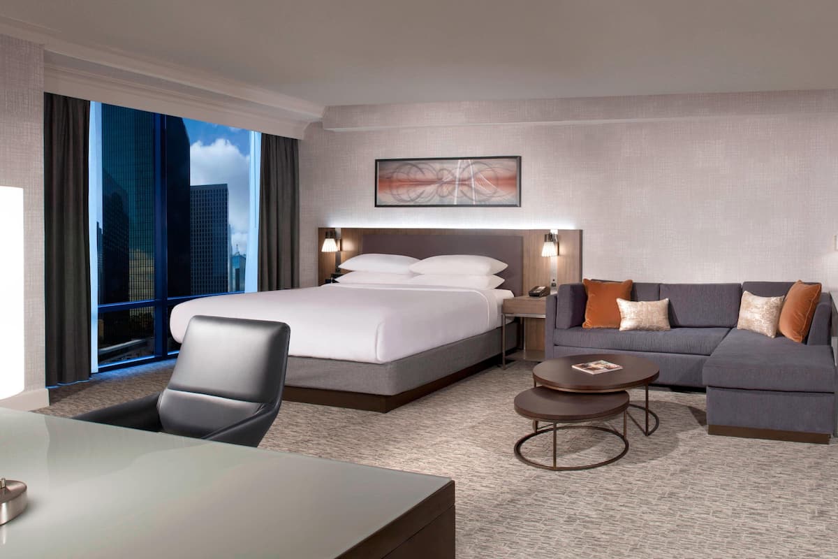 A modern hotel room with a large bed, a sofa, a desk, and a view of the cityscape.