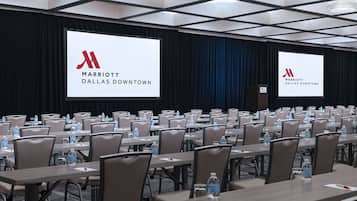 Un salón de conferencias con filas de mesas, sillas y pantallas grandes mostrando el logotipo de Marriott Dallas Downtown.