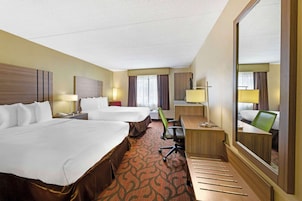 Quarto de hotel com duas camas, uma escrivaninha, uma cadeira, um espelho e uma janela grande.