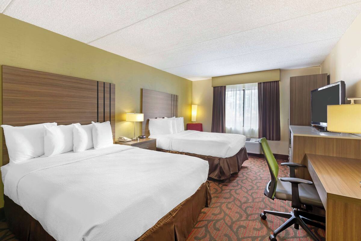 A hotel room with two beds, a desk, a chair, a TV, and a window with curtains.