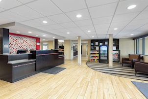 Uma área de recepção com balcão de check-in, espaço de espera com sofás, máquina de vendas automática e frigorífico.