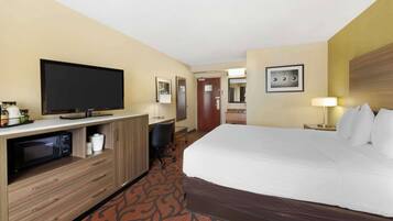 A hotel room with a large bed, a flat-screen TV, a desk with a chair, a microwave, and a small kitchenette.