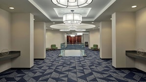 Un hall d’hôtel spacieux, doté d’un tapis aux motifs géométriques, de plusieurs lustres et d’une rambarde centrale en verre donnant sur un espace salon.