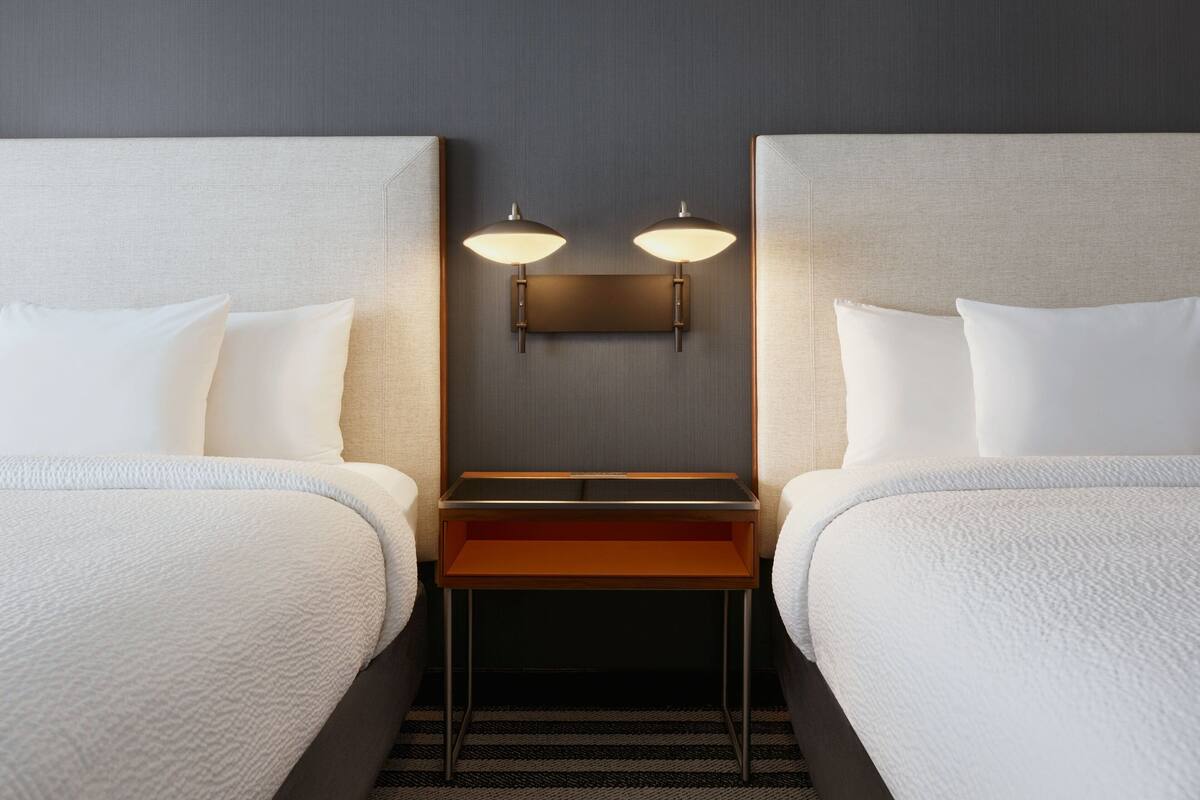 A hotel room with two beds, a small table, and a wall-mounted light fixture.