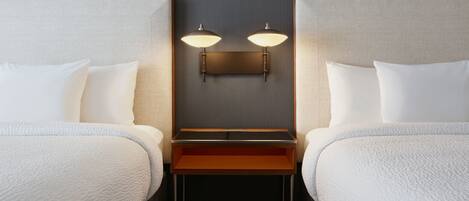 A hotel room with two beds, a small table, and a wall-mounted light fixture.