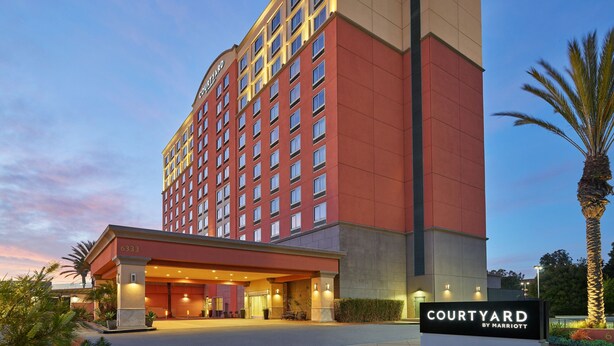 Un hôtel à plusieurs étages, reconnaissable à son grand panneau « Courtyard by Marriott », qui présente une architecture moderne avec une façade rouge et beige, ainsi qu’un hall d’entrée bien éclairé.