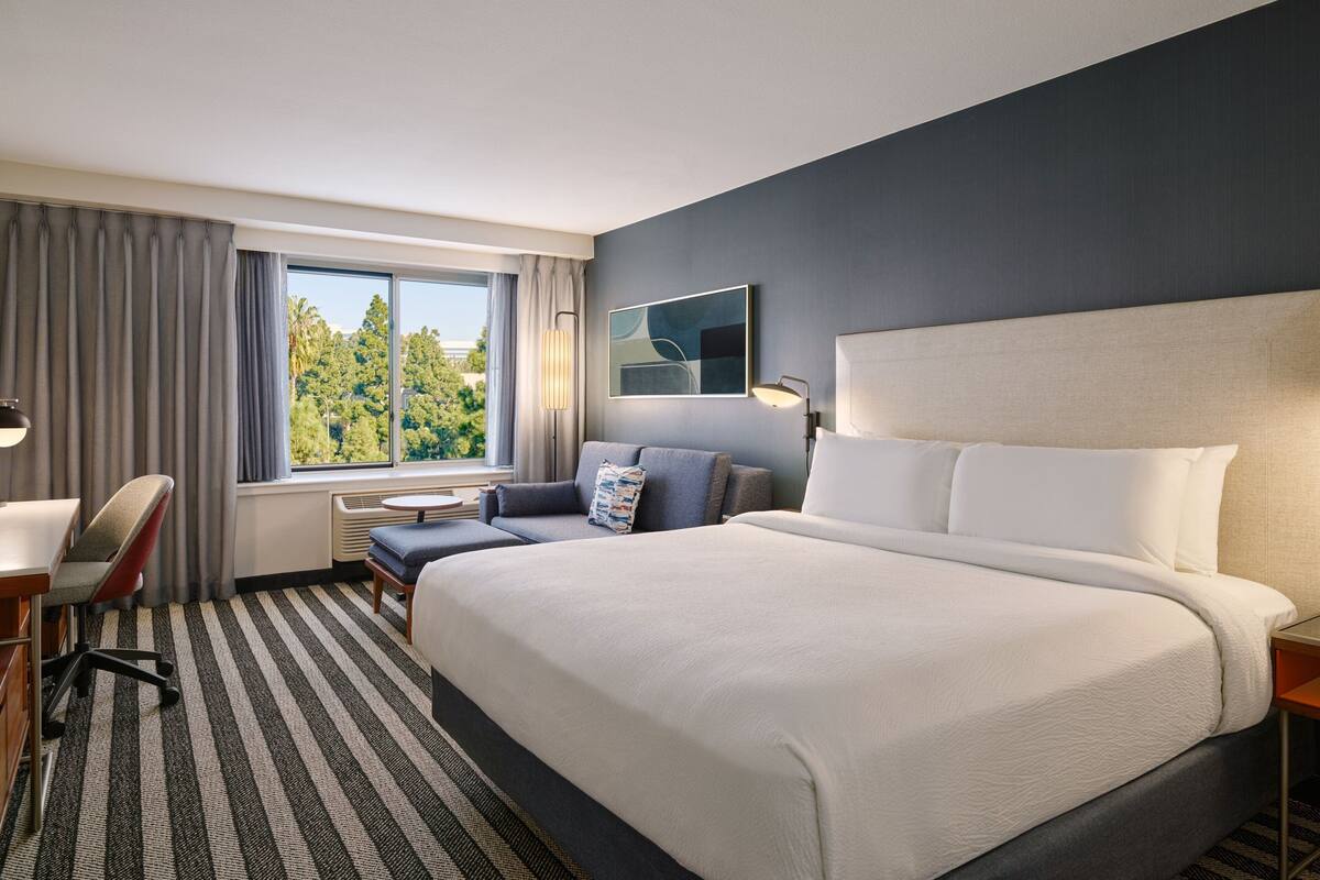 A hotel room with a large bed, a desk, a chair, a sofa, and a window with curtains.