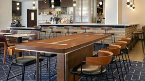 Un espace bar moderne avec un long comptoir en bois, de nombreux tabourets et des luminaires suspendus.