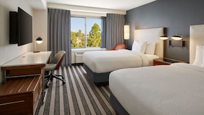 Une chambre d’hôtel avec deux lits, un bureau, une chaise, un téléviseur à écran plat et une fenêtre avec des rideaux.