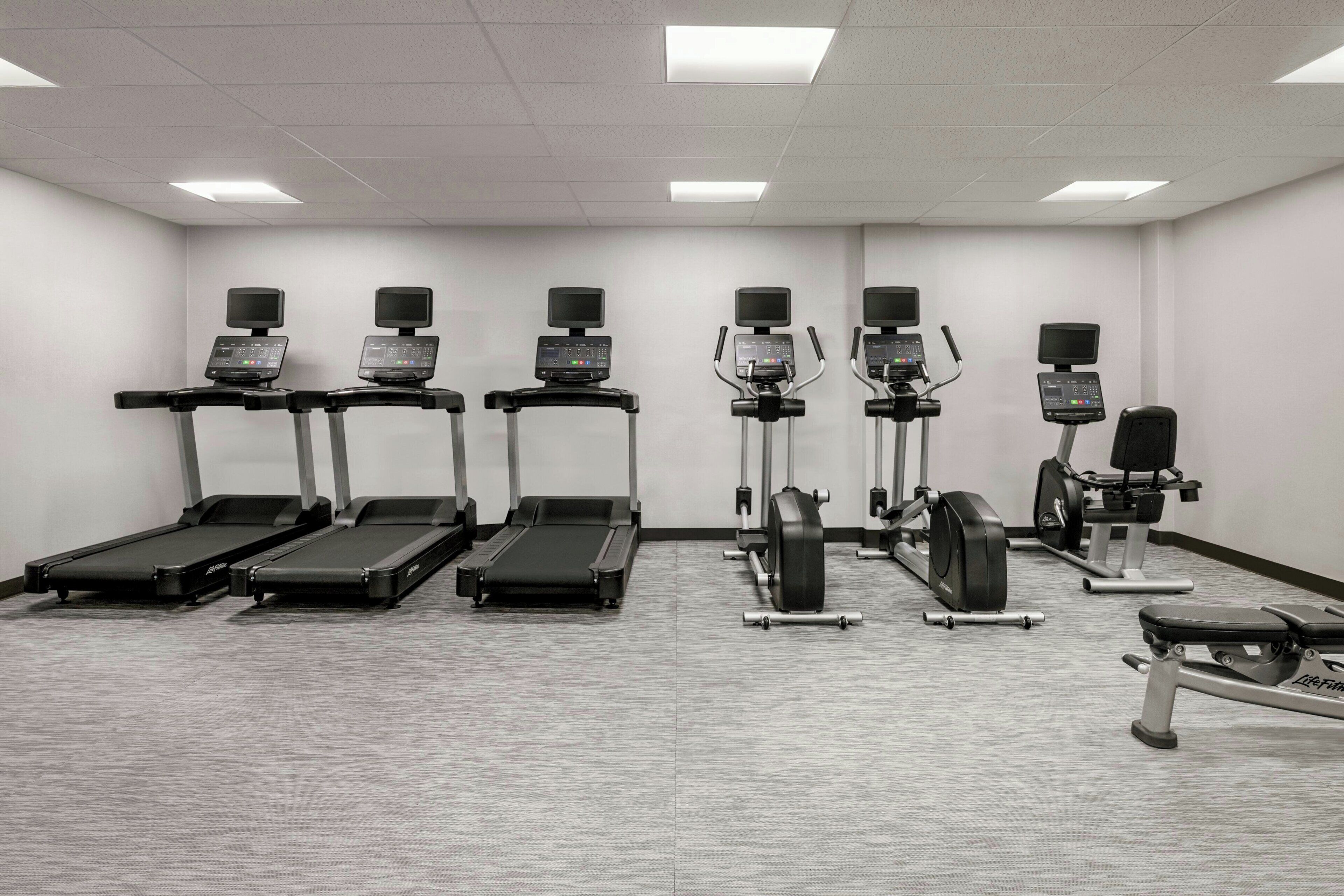 Un gimnasio con cintas de correr, elípticas y una bicicleta estática.