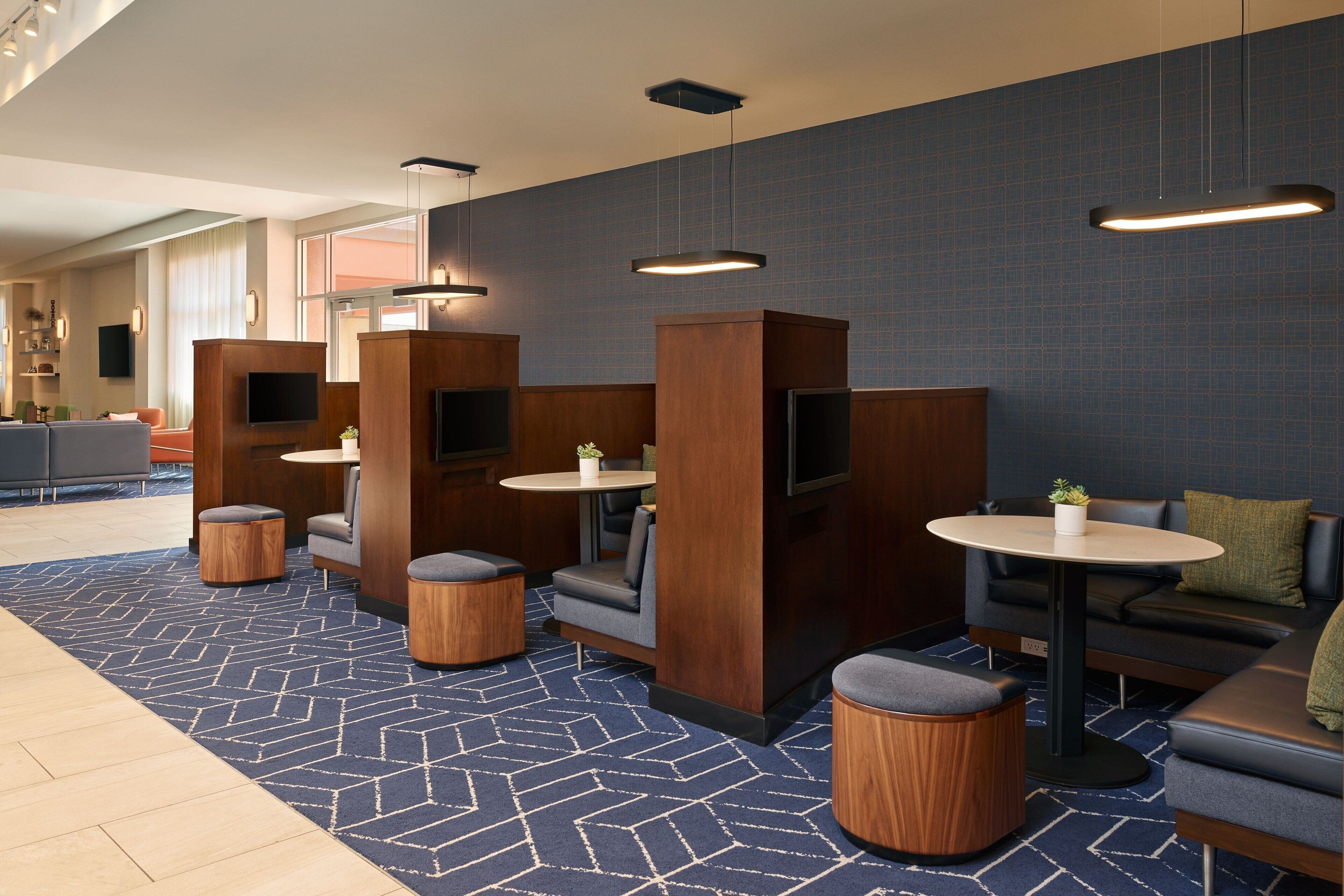 Un hall d’hôtel moderne, doté d’espaces aménagés avec des sièges, de cloisons en bois et d’un tapis à motifs.