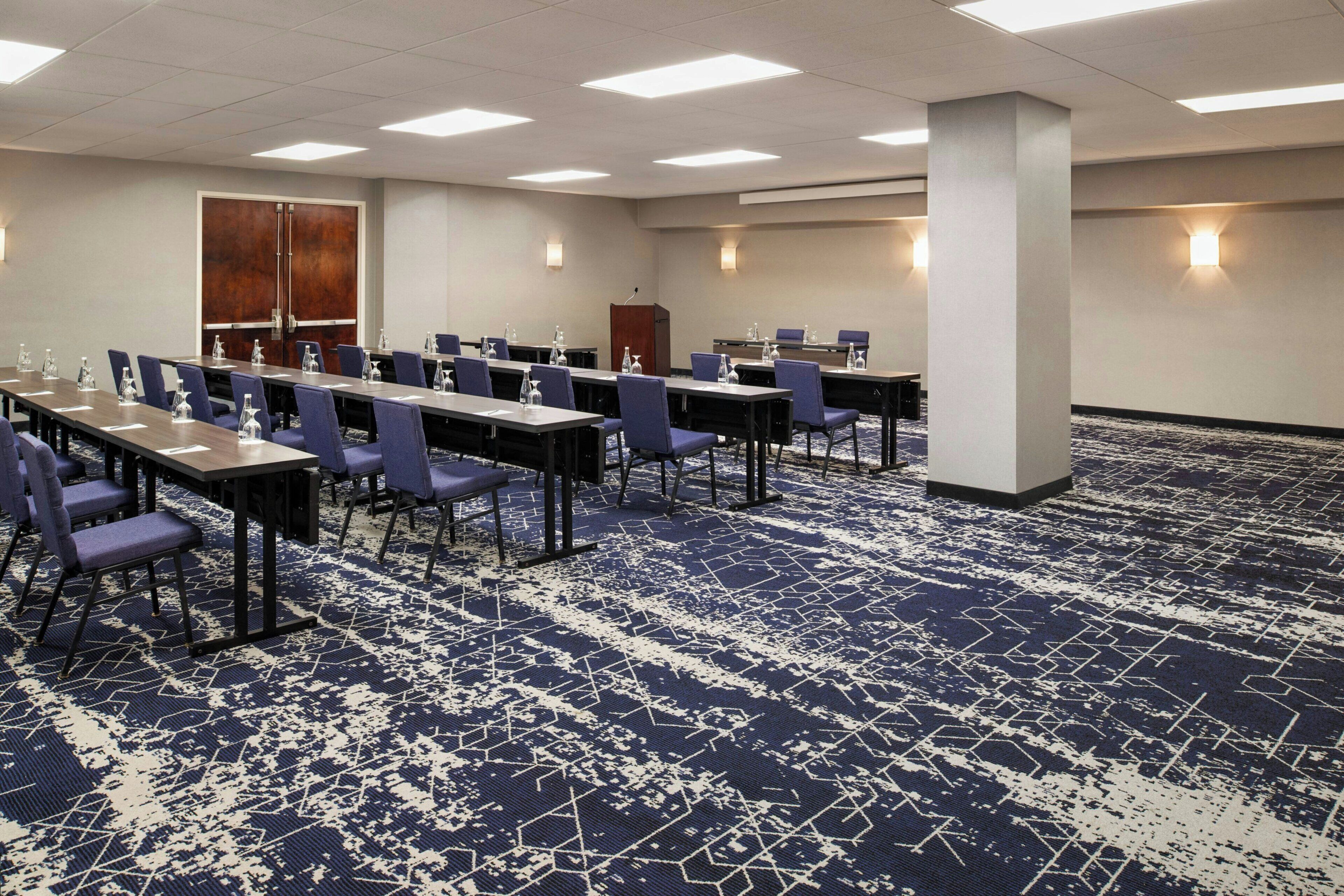 Une salle de conférence dotée de plusieurs tables et de chaises, ainsi que de bouteilles d’eau et de blocs-notes.