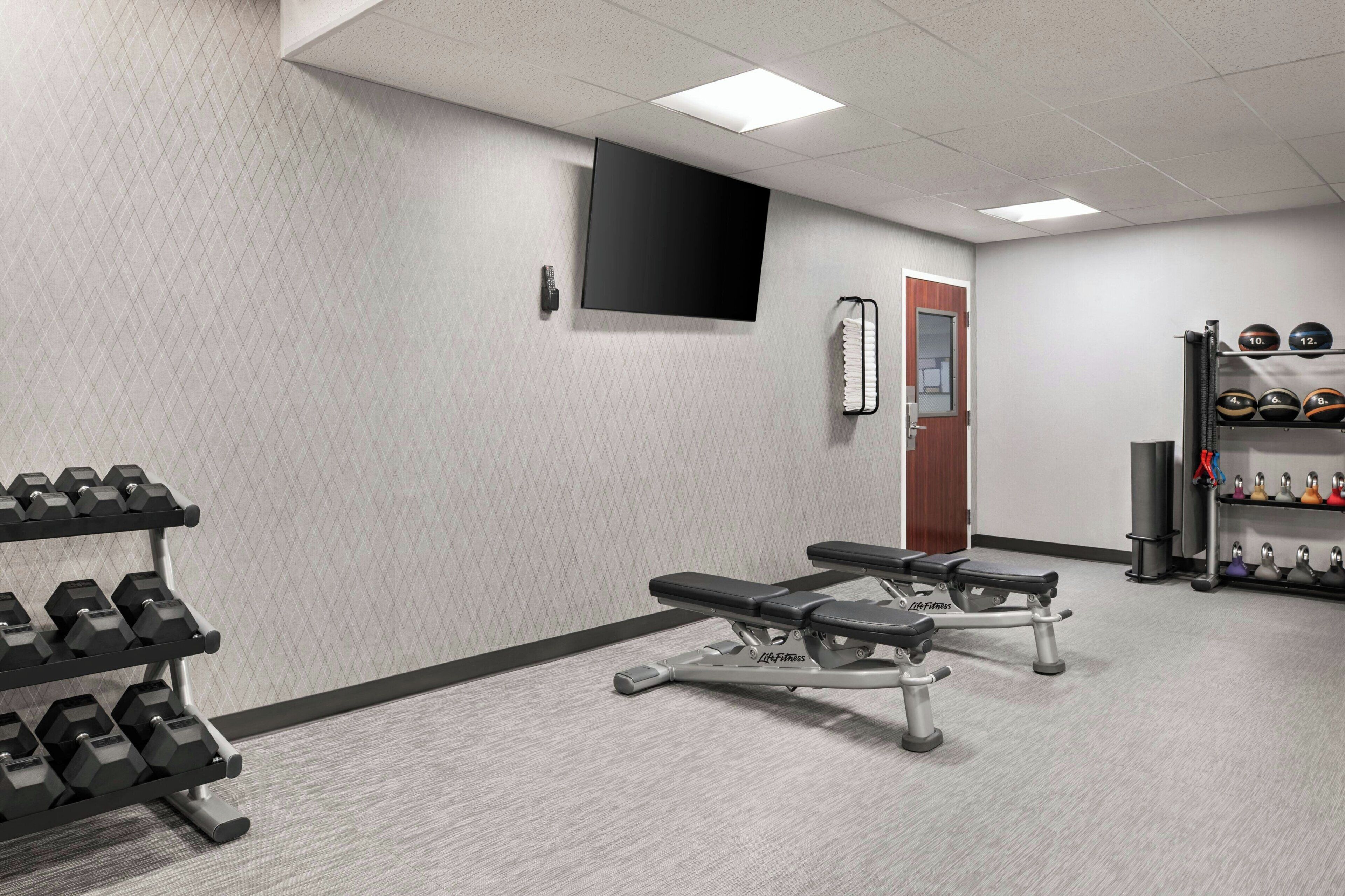 A gym with weightlifting equipment, benches, and a wall-mounted TV.