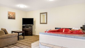 A hotel room with a sofa, a flat-screen TV, a small table, a red bathtub, and a mirror on the wall. - Quality Inn Huntingburg - Jasper (Huntingburg)