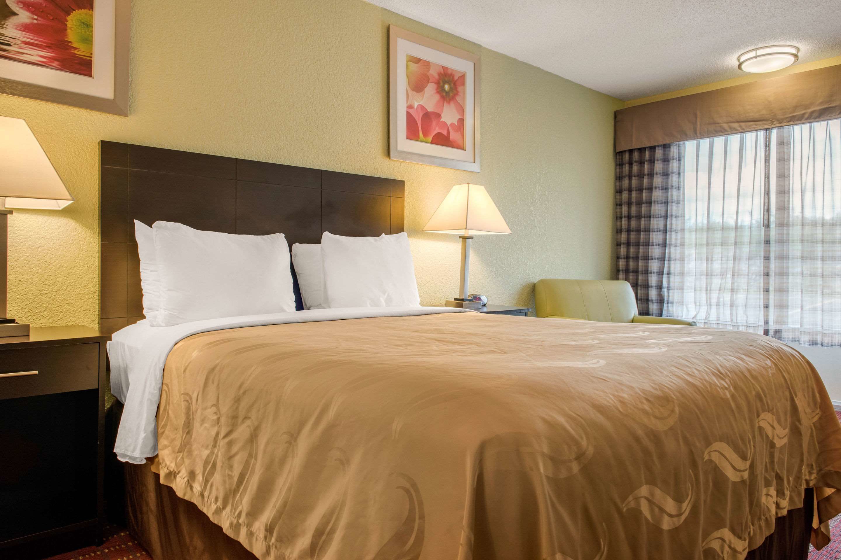A hotel room with a large bed, two bedside lamps, a nightstand, a chair, and a window with curtains.