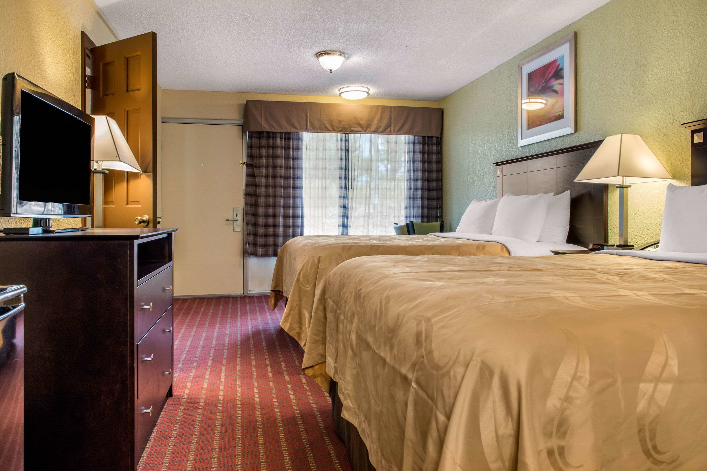 A hotel room with two beds, a TV, a desk, and a window with curtains.