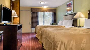 A hotel room with two beds, a TV, a desk, and a window with curtains.