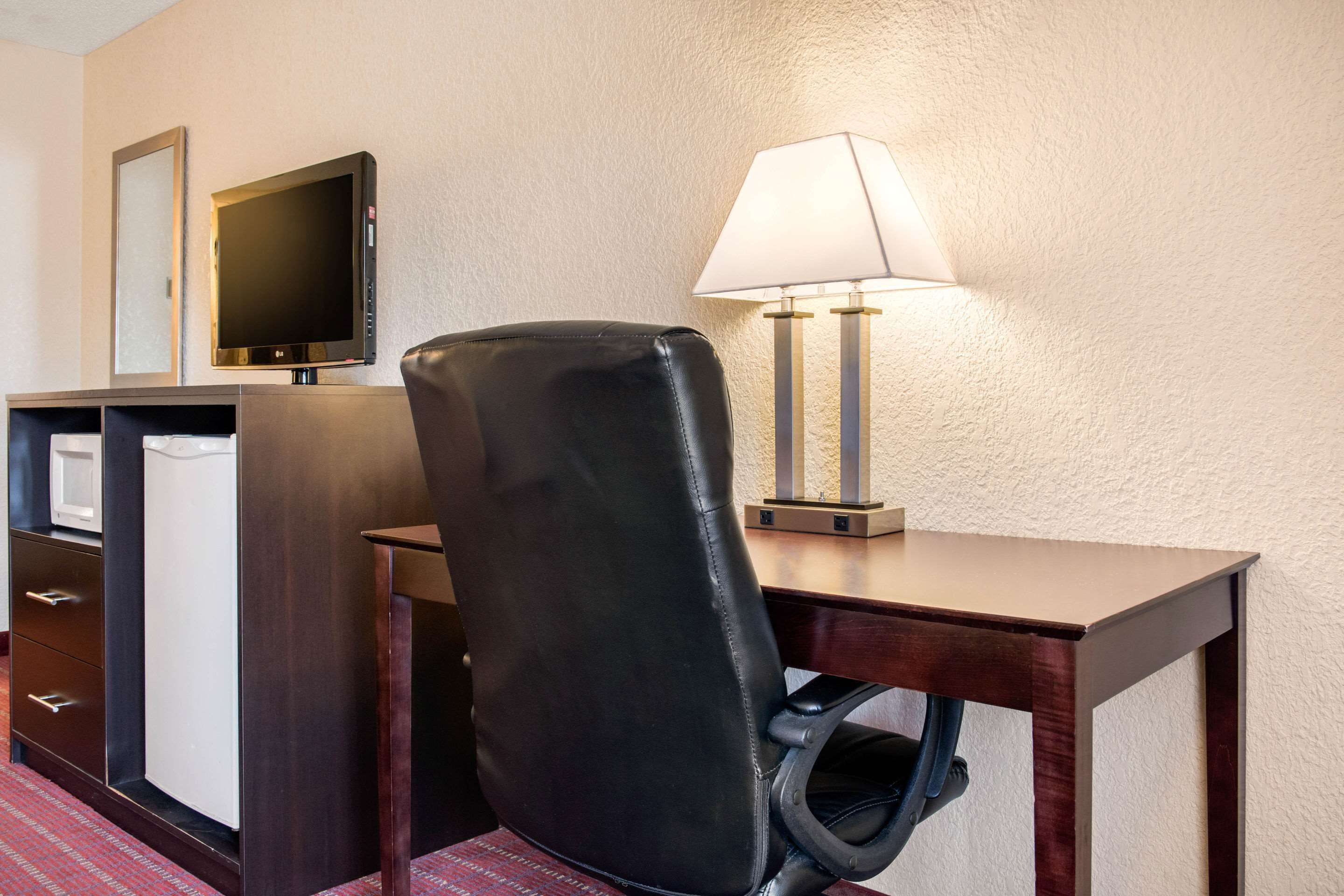 A hotel room with a desk, a chair, a television, a lamp, and a minibar.