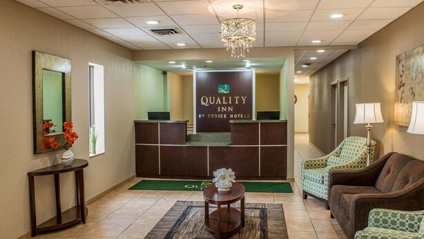A hotel reception area with a reception desk, a chandelier, a green carpet, and a couch. - Quality Inn Huntingburg - Jasper (Huntingburg)