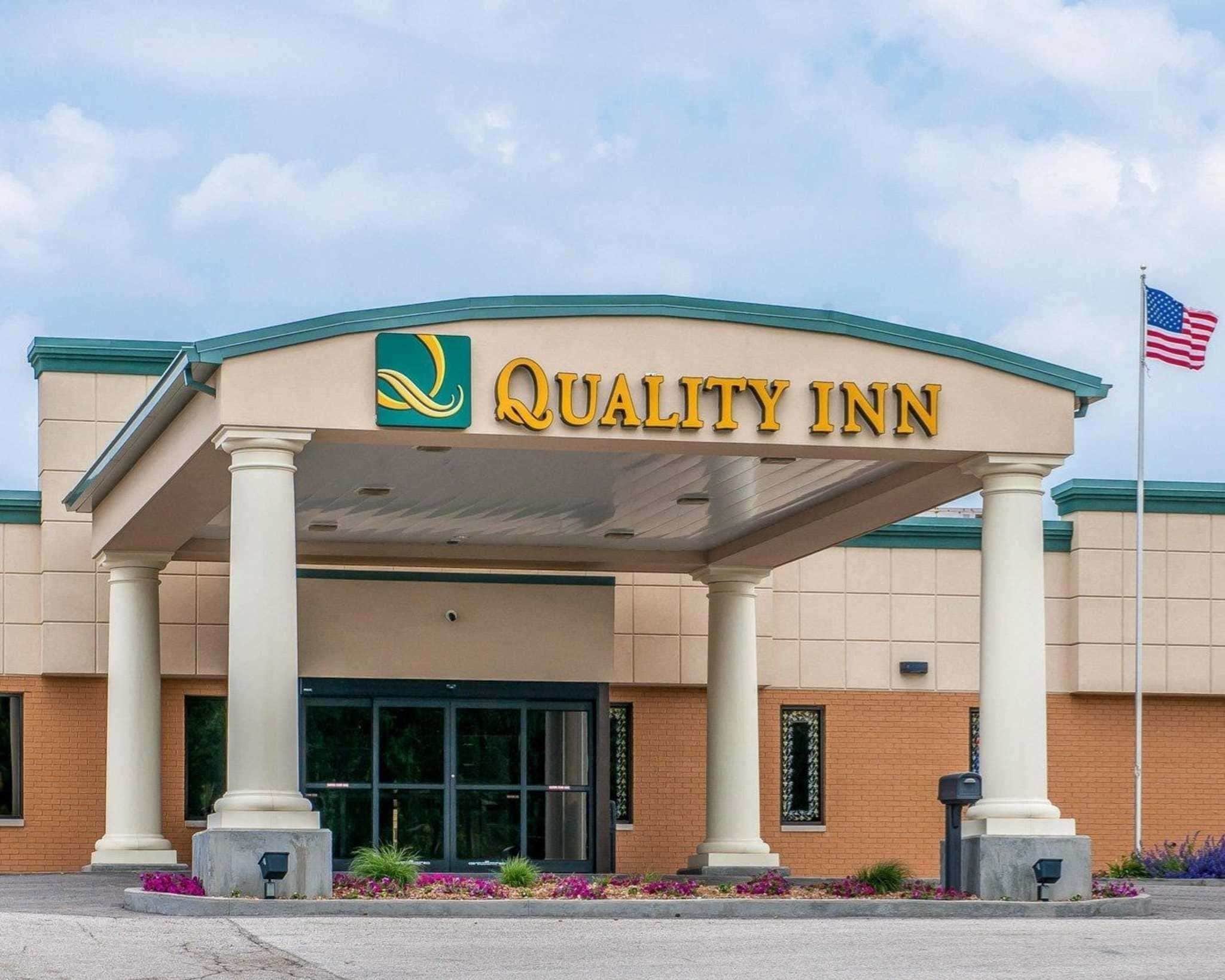 A Quality Inn hotel entrance with a covered walkway, columns, and an American flag.
