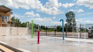 A water feature with multiple jets in different colors, a paved area, and a fence in the background. - Quality Inn Huntingburg - Jasper (Huntingburg)