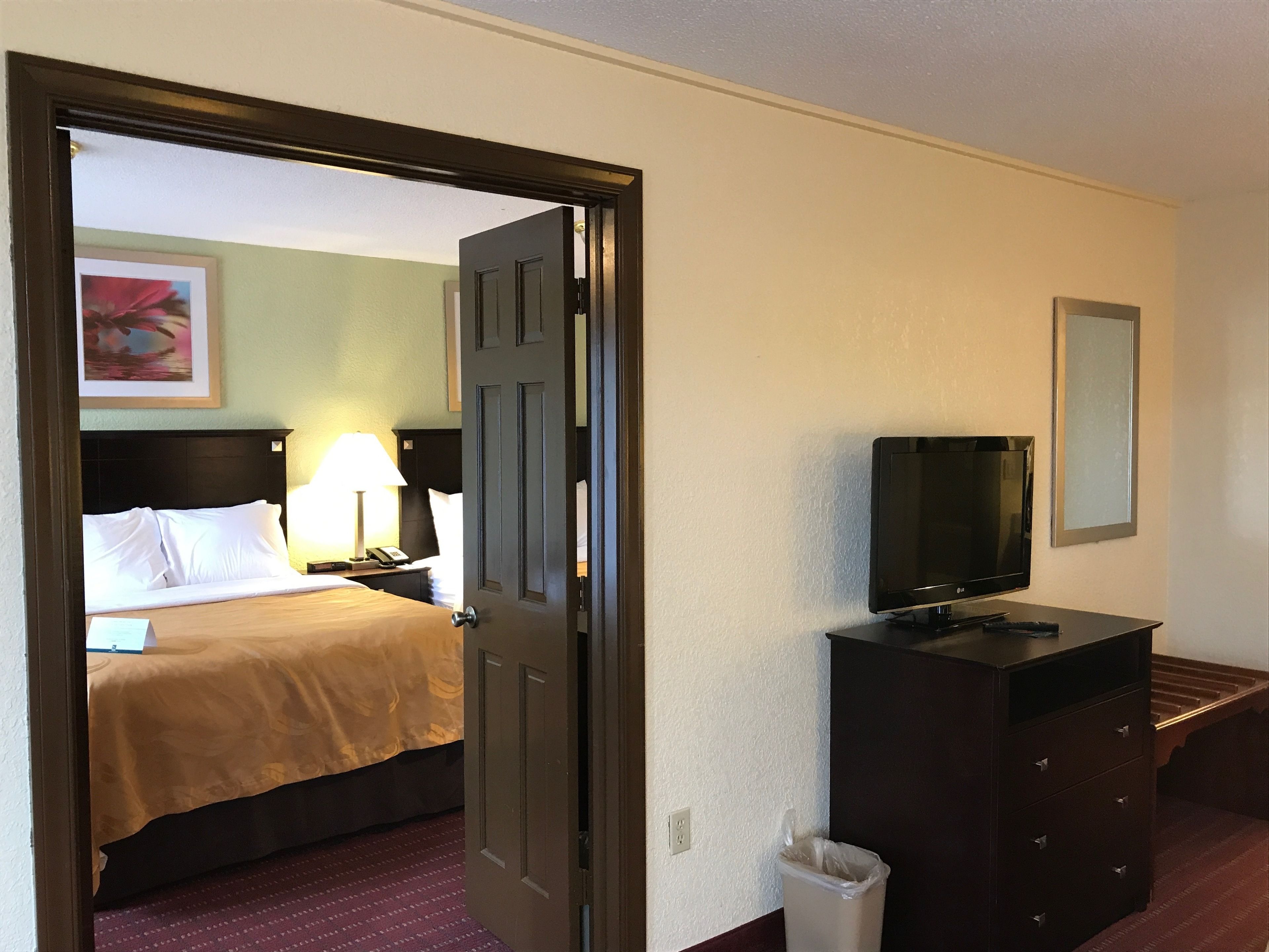 A hotel room with a bed, a dresser, a television, and a trash can.