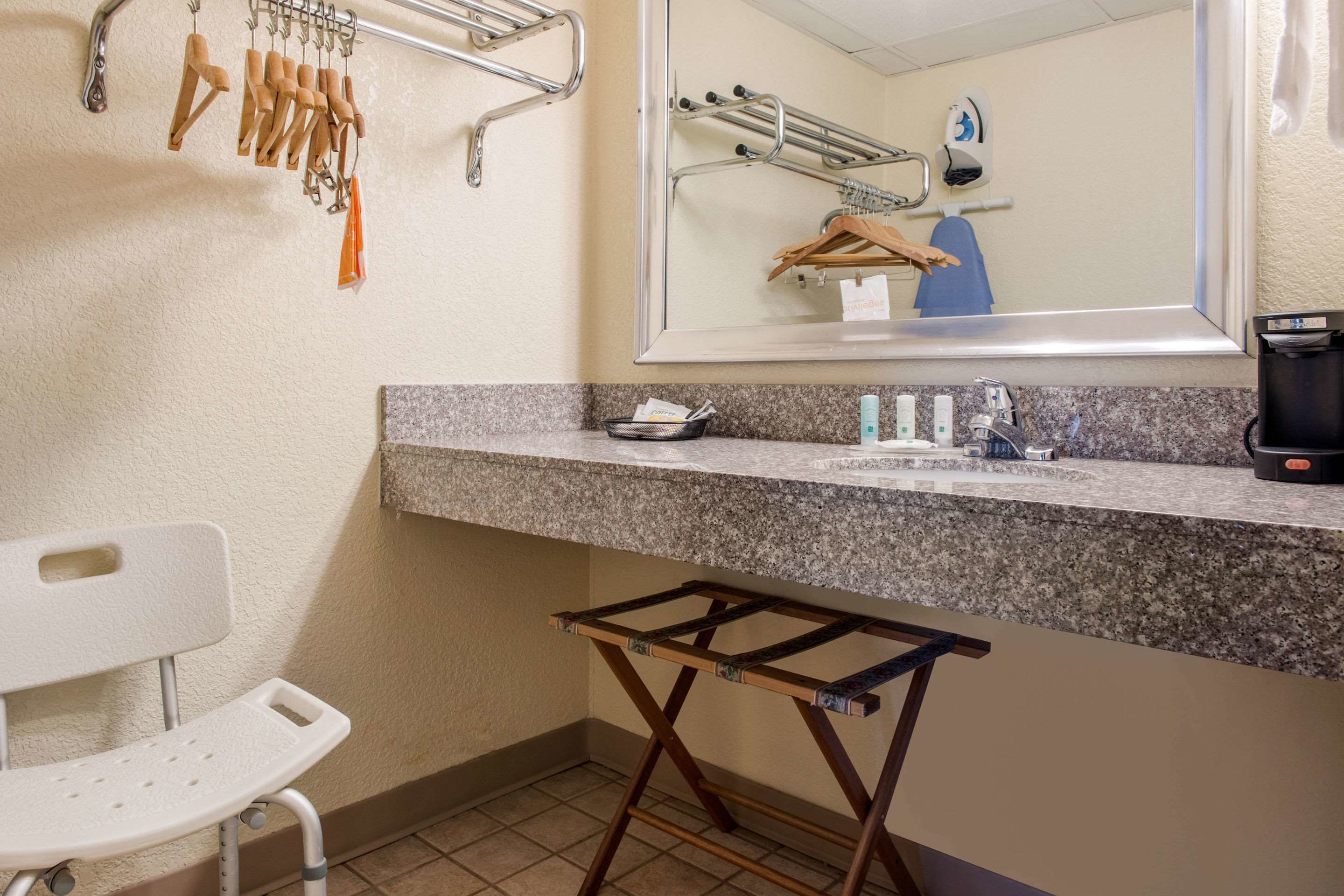 A bathroom with a granite countertop, a sink, a mirror, a towel rack, and a drying rack.