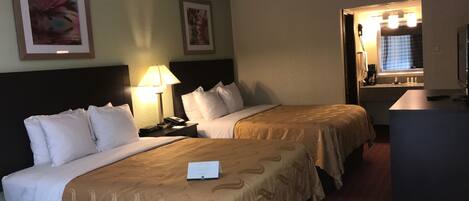 A hotel room with two beds, a desk, a chair, a trash bin, and a window with curtains.