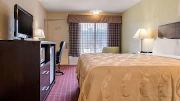 Une chambre d’hôtel avec un lit, un bureau avec un ordinateur, une télévision et une fenêtre avec des rideaux.