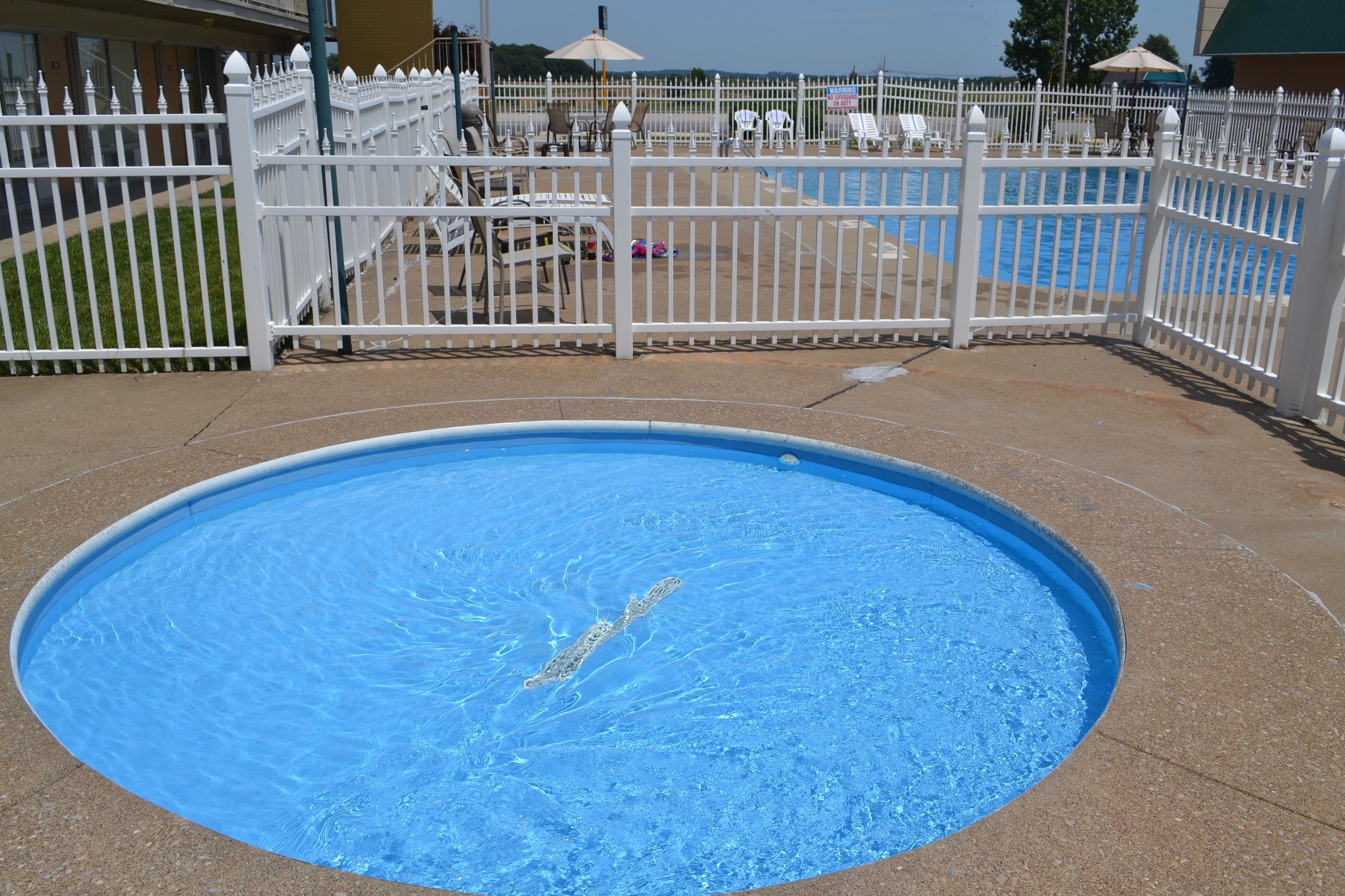 Una piscina con una cerca blanca y sillas de descanso al fondo.